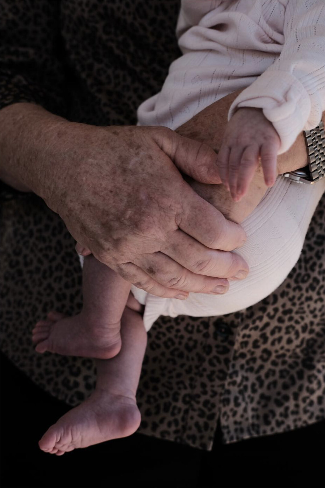 A grandparent's hand holding a baby's arm and leg